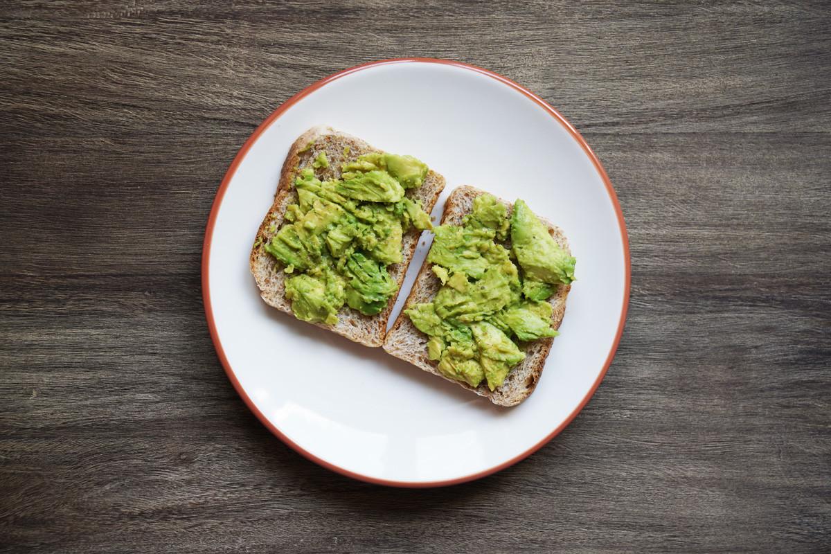 Two Slices of Avocado Toast on a Plate on Rustic Wooden Table